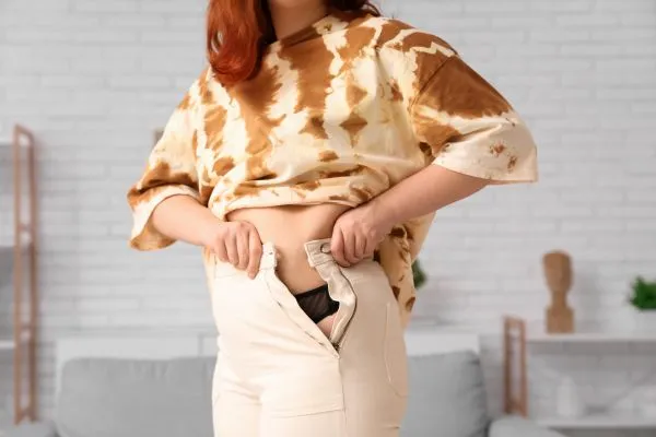 Image of woman trying to do her trousers up after pregnancy weight gain Pinner
