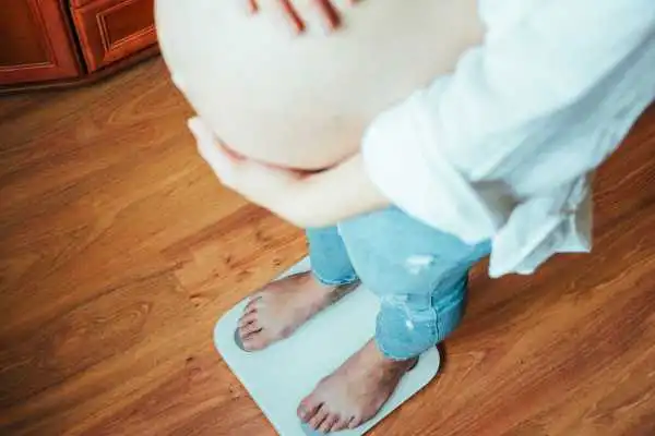 Image of woman weighing herself and experiencing weight gain through pregnancy Pinner
